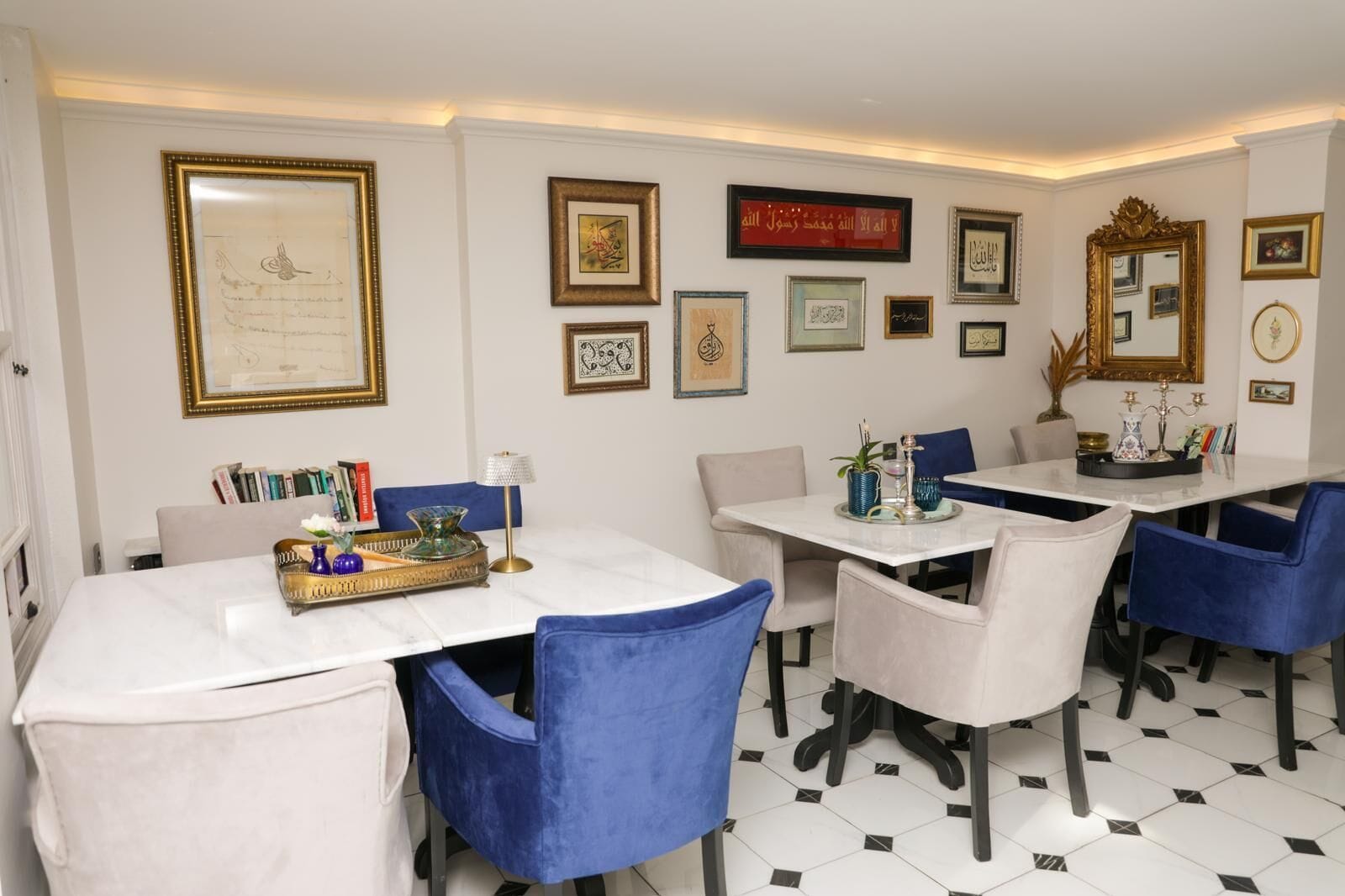 A dining area with white marble tables, blue upholstered chairs, and a variety of framed calligraphy and artwork on the walls.