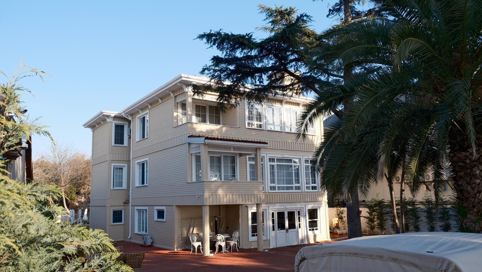 Un edificio de varios pisos con techo plano, ventanas grandes y un espacio al aire libre cubierto con sillas.
