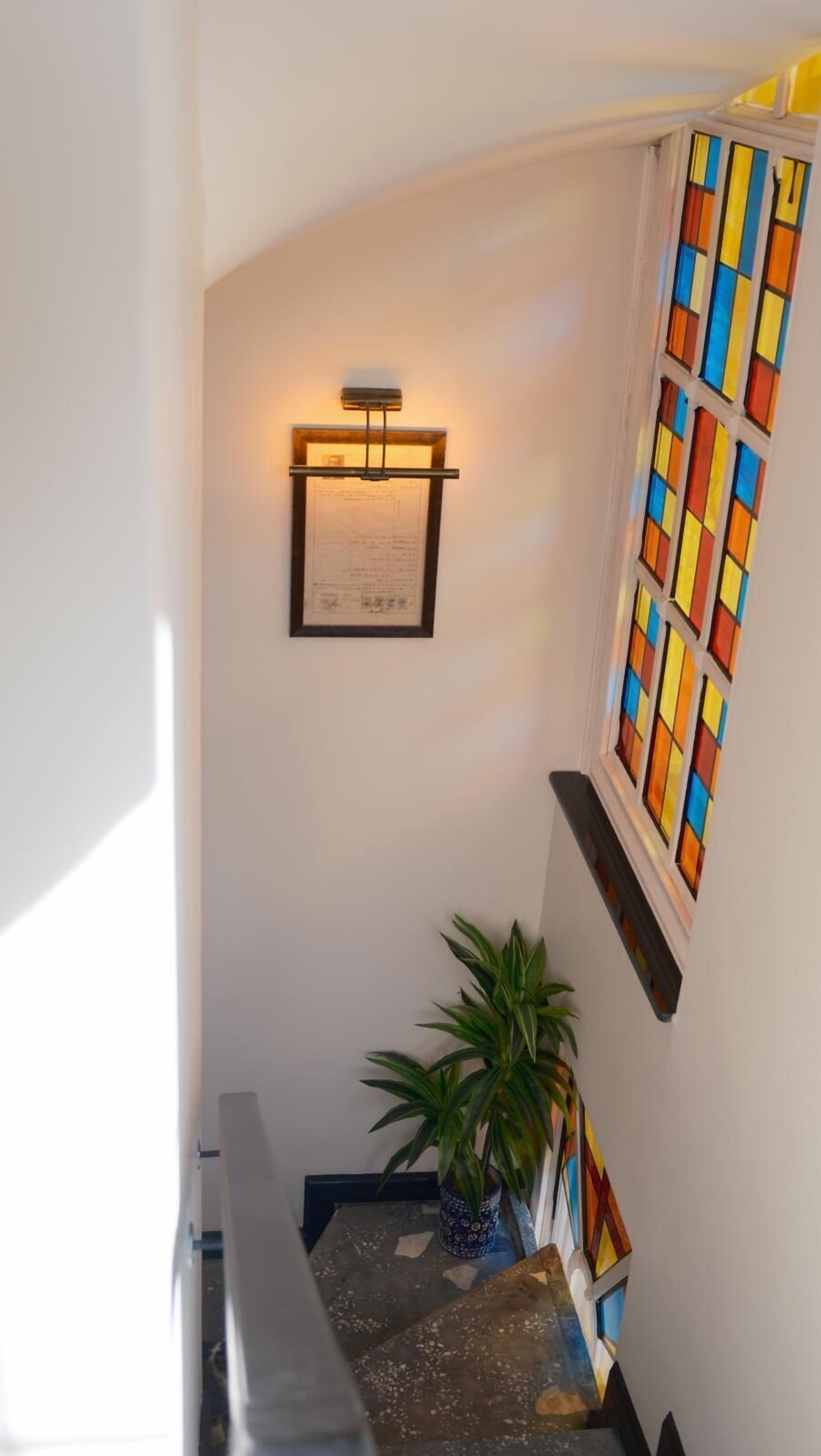 Una escalera con un certificado enmarcado, una planta en maceta y un ventanal de vidrio con vidrieras de colores.