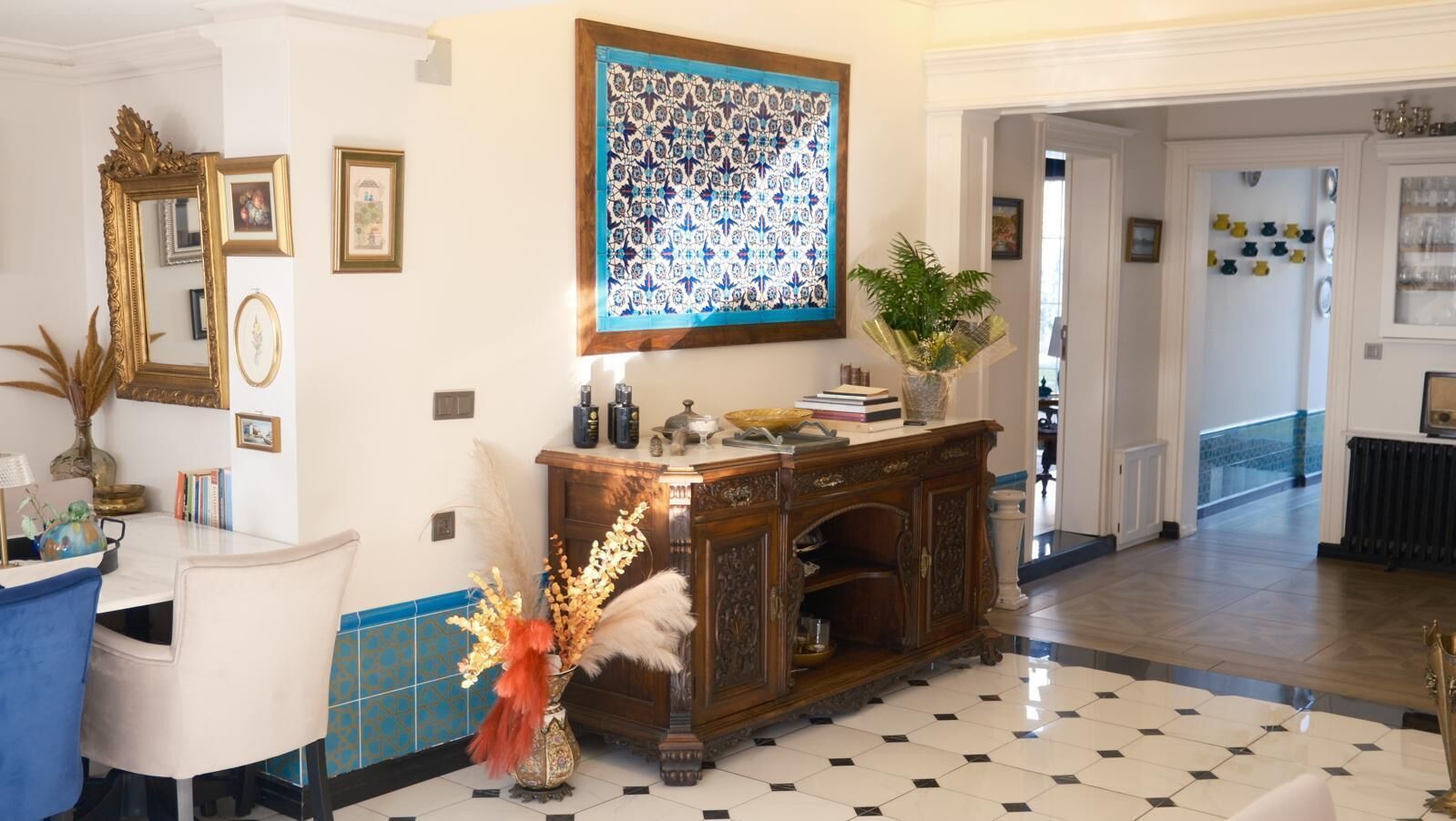 Una habitación con una mesa de comedor, sillas, un aparador decorativo, una obra de arte grande enmarcadas y una planta en maceta.