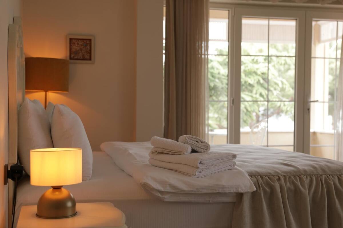 A neatly made bed with folded towels, a bedside lamp, and a window with curtains.