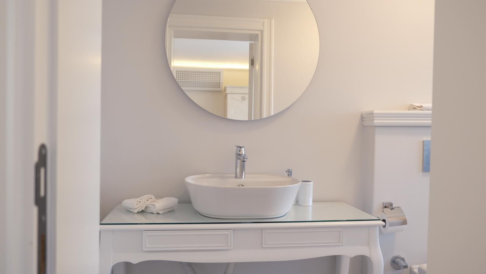 Een badkamer met een ronde spiegel, een witte wastafel, een handdoek en een toiletpapierhouder.
