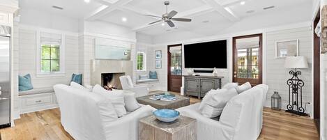 A spacious living room with white furniture, a fireplace, and a large TV.