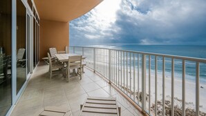 A balcony with a view of the beach and ocean, a table with chairs, and a glass door leading to an interior space. - Phoenix Gulf Towers 1106 2 Bedroom Condo (Orange Beach)