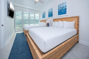 A bedroom with two beds, a TV, artwork, and a view of the ocean.