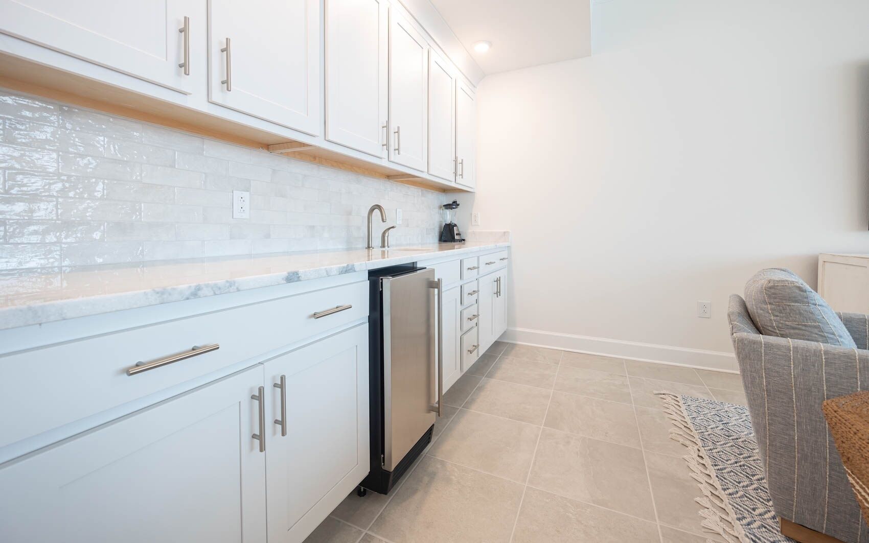 A modern kitchen with white cabinetry, a marble backsplash, and a built-in dishwasher.