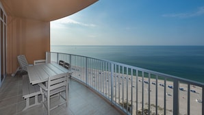 Varanda com mesa e cadeiras, vista para uma praia com guarda-sóis.