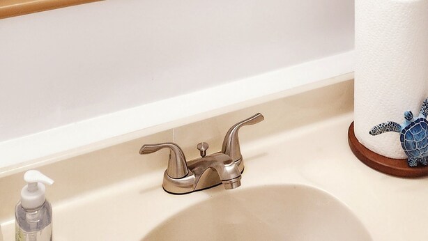 Een badkamer met een decoratief wandobject, een wastafel, een kraan, een zeepdispenser en een toiletrolhouder.