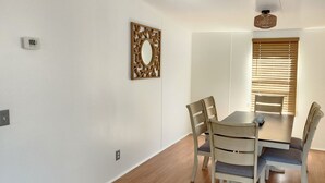 Een eetgedeelte met een tafel en vier stoelen, een decoratieve spiegel en een raam met jaloezieën.