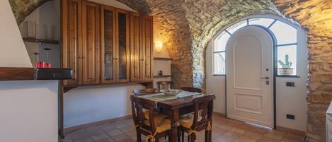 A stone-walled kitchen with wooden cabinets, a dining table with chairs, and a door leading to a patio.