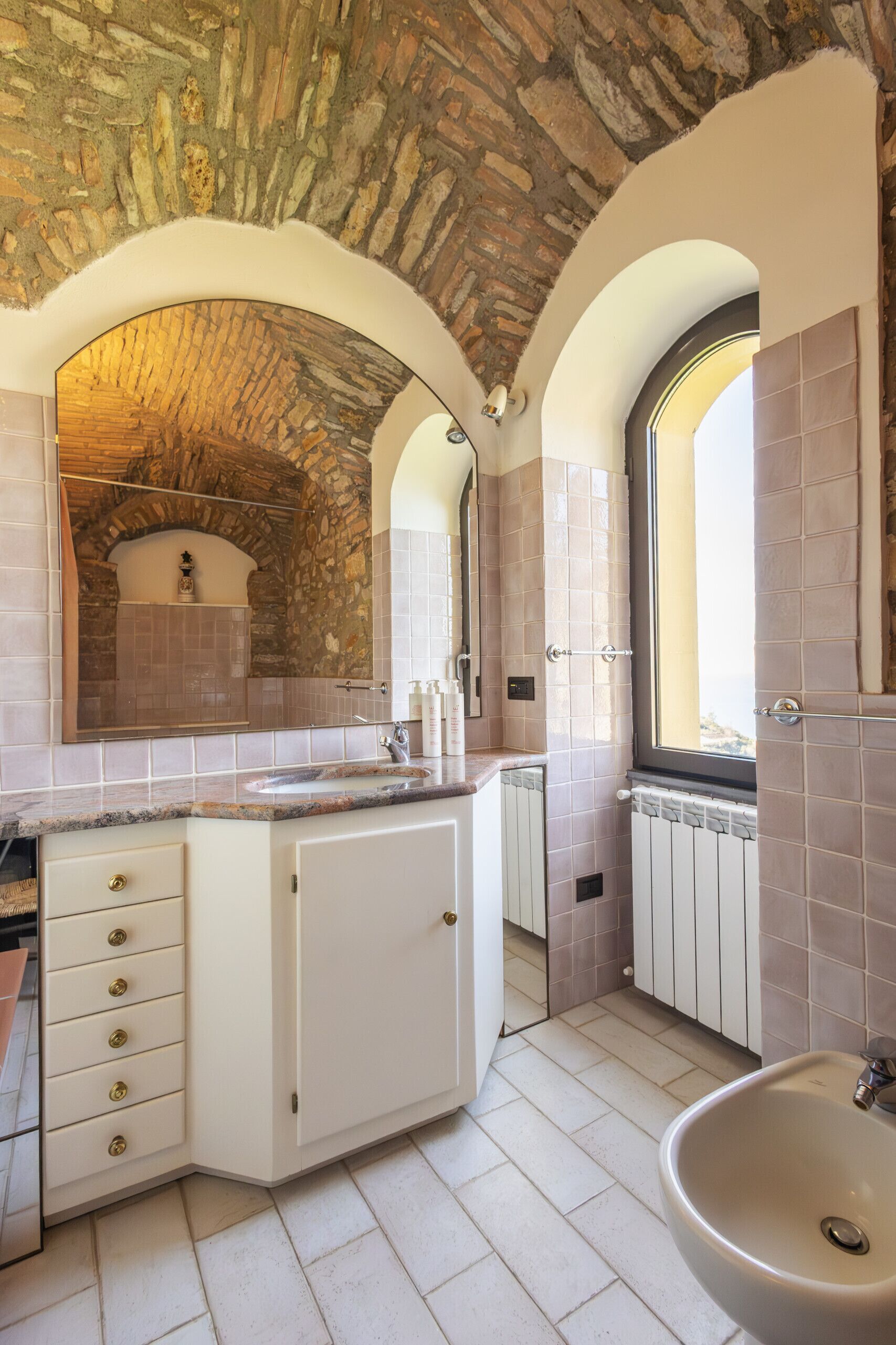 Une salle de bain avec un plafond en forme d’arc en pierre, un grand miroir, un lavabo et une fenêtre.