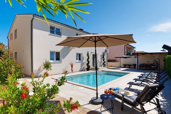 A swimming pool with lounge chairs and a table, surrounded by a building with a tiled patio. - Villa Nata in Pula - Haus für 8 Personen (Pula)