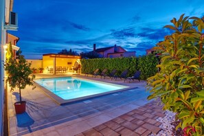 A swimming pool with lounge chairs and a patio area, surrounded by greenery and buildings. - Villa Nata in Pula - Haus für 8 Personen (Pula)