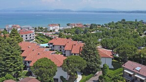 Un quartier résidentiel situé sur la côte, caractérisé par des toits recouverts de tuiles rouges, de nombreux arbres verdoyants et une vue sur la mer.