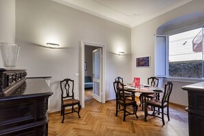 Un comedor con piso de madera en patrón de espiga, una mesa preparada para cuatro personas y una ventana con vista a un edificio.