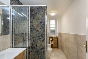 Un baño moderno con cabina de ducha de vidrio, lavamanos blanco, inodoro y tocador de madera.
