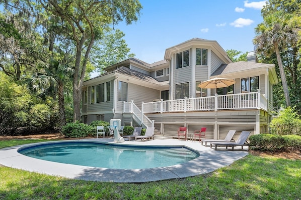 A two-story house with a swimming pool, a covered deck, and a staircase leading to a balcony.