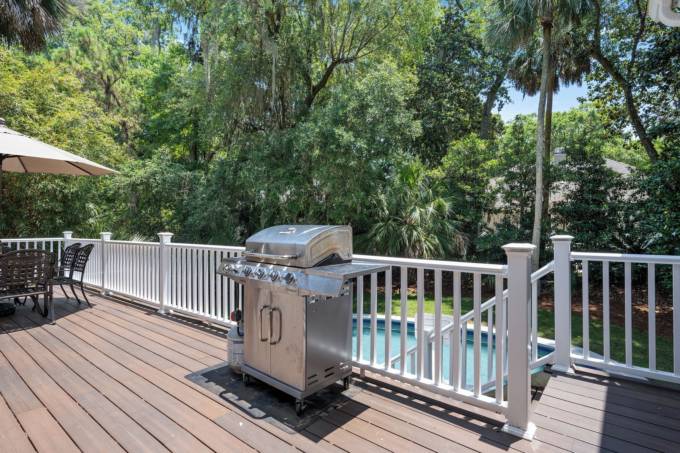 Eine Terrasse mit Grill, Pool und weißer Geländer.