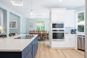 A modern kitchen with white cabinets, a central island, and a dining area with wooden chairs.