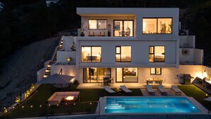 A modern two-story house with a swimming pool, outdoor seating, and large windows.