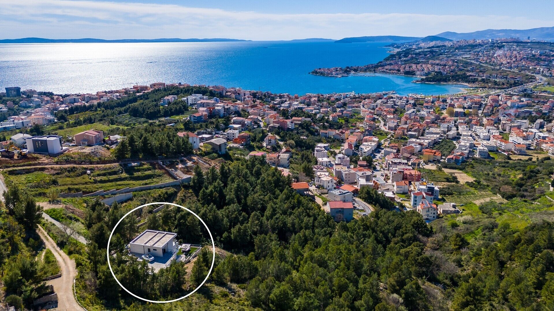 Luftaufnahme einer Küstenstadt mit Wohnhäusern und offenen Flächen, einem großen Gewässer und einem markierten Bereich, der einen bestimmten Ort kennzeichnet.