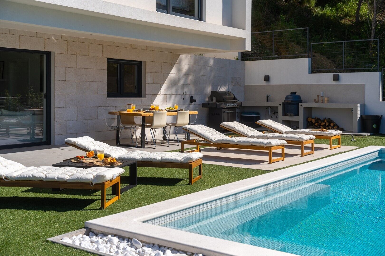A modern outdoor pool area with lounge chairs, a dining table, and a barbecue grill.