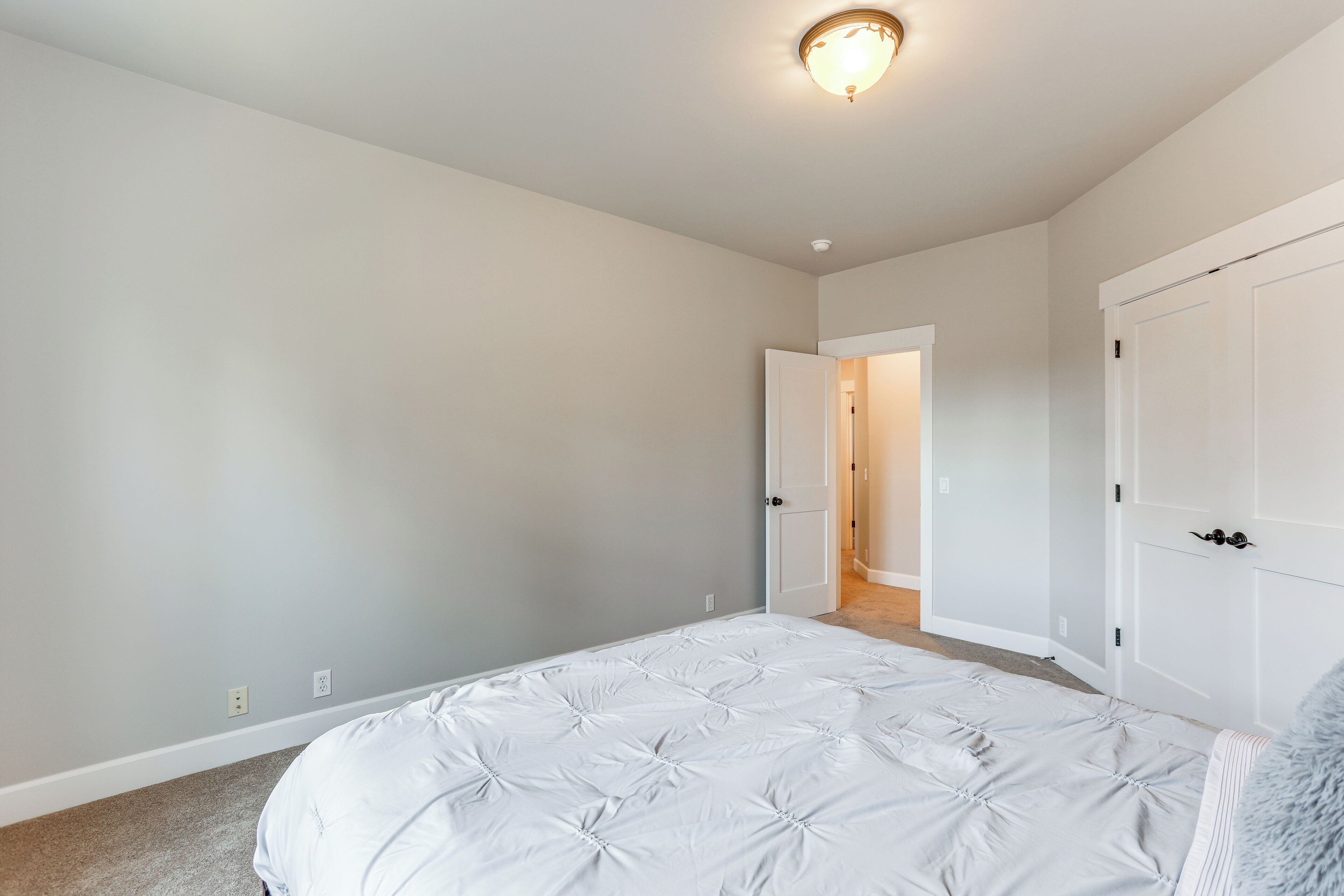 A bedroom with a large bed, white walls, and a door leading to another room.