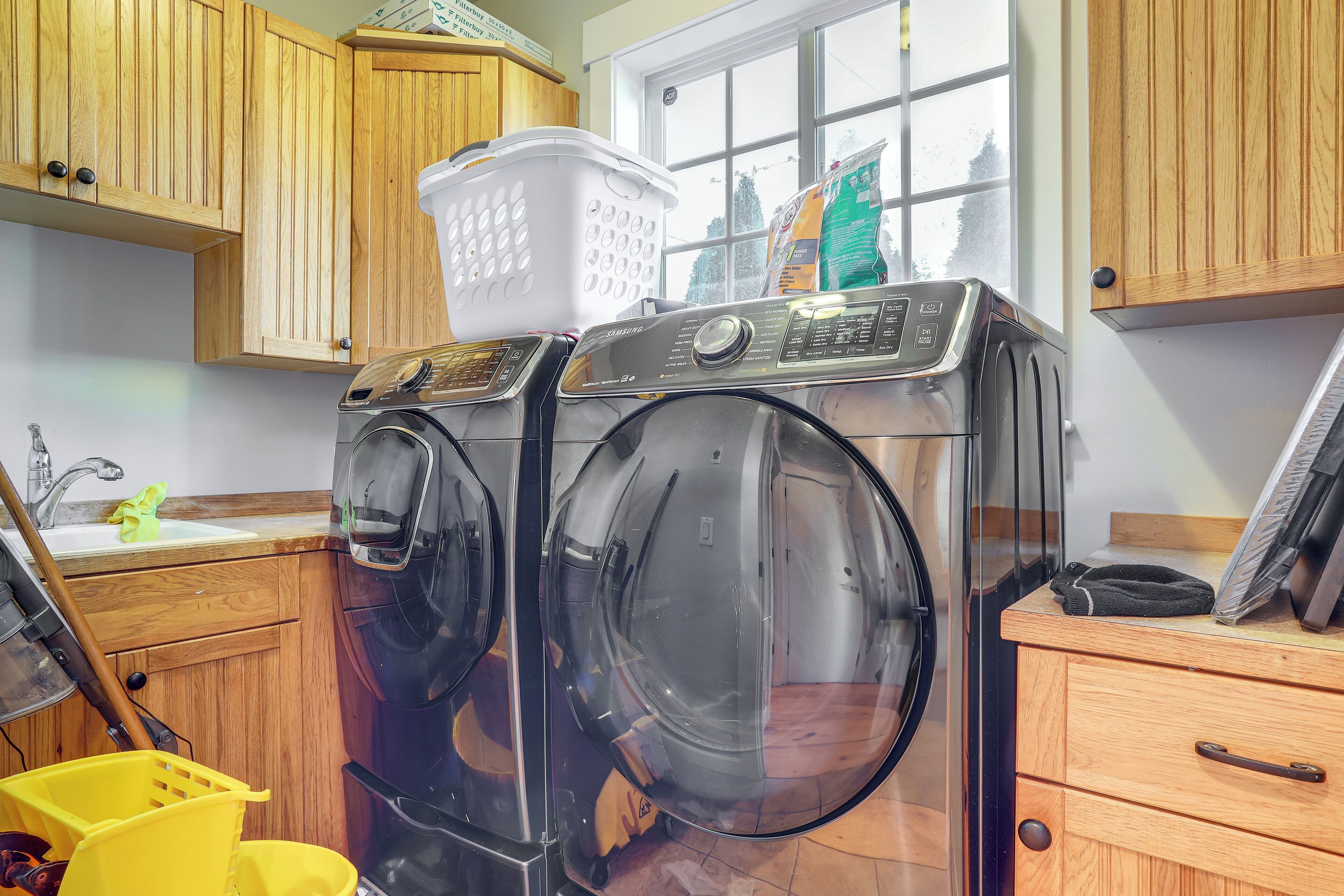 A laundry area with two front-loading washing machines, wooden cabinets, a window, and a yellow laundry basket.