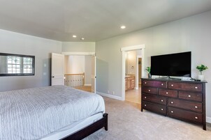 Quarto com cama, penteadeira, televisão e porta para um banheiro.