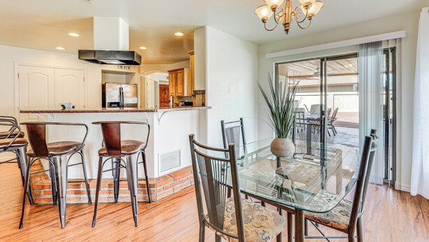 A dining area with a glass table and metal chairs, a kitchen with white cabinets, and a large window with a view. - Private Pool & Patio: Home Near Mesa Arts Center! (Mesa)