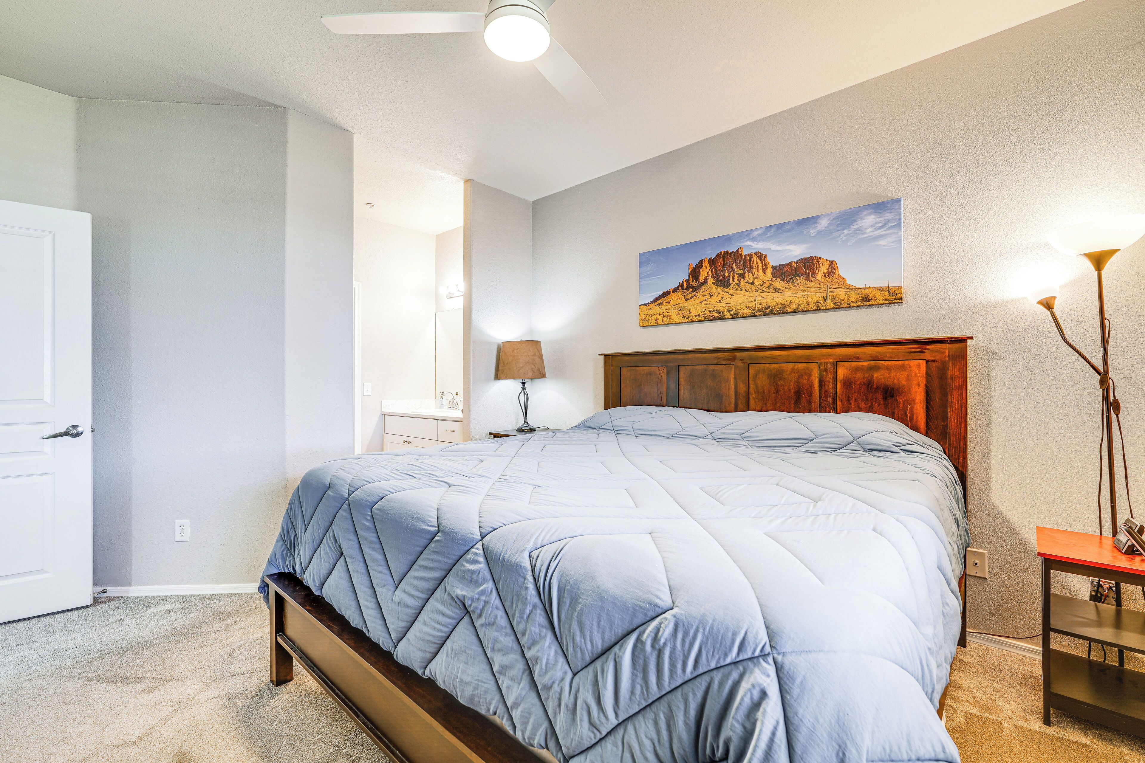 A bedroom with a bed, a wooden headboard, a painting on the wall, a lamp, and a door.