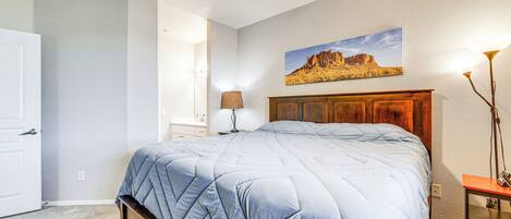 A bedroom with a bed, a wooden headboard, a painting on the wall, a lamp, and a door.