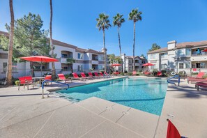 A pool area with red lounge chairs and umbrellas, surrounded by palm trees and a building with balconies. - Pool Access, Near Spring Training! Mesa Retreat (Mesa)