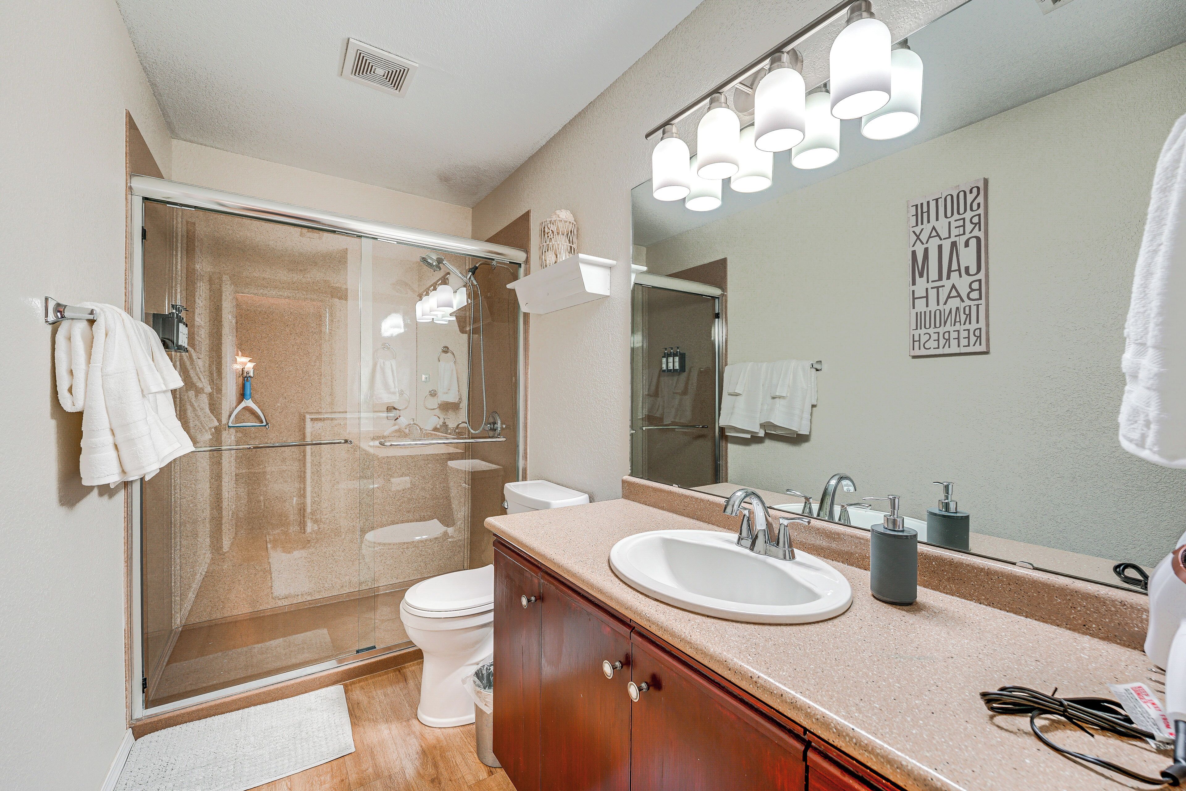 A modern bathroom with a glass shower enclosure, a white toilet, a vanity with a sink, and a large mirror.