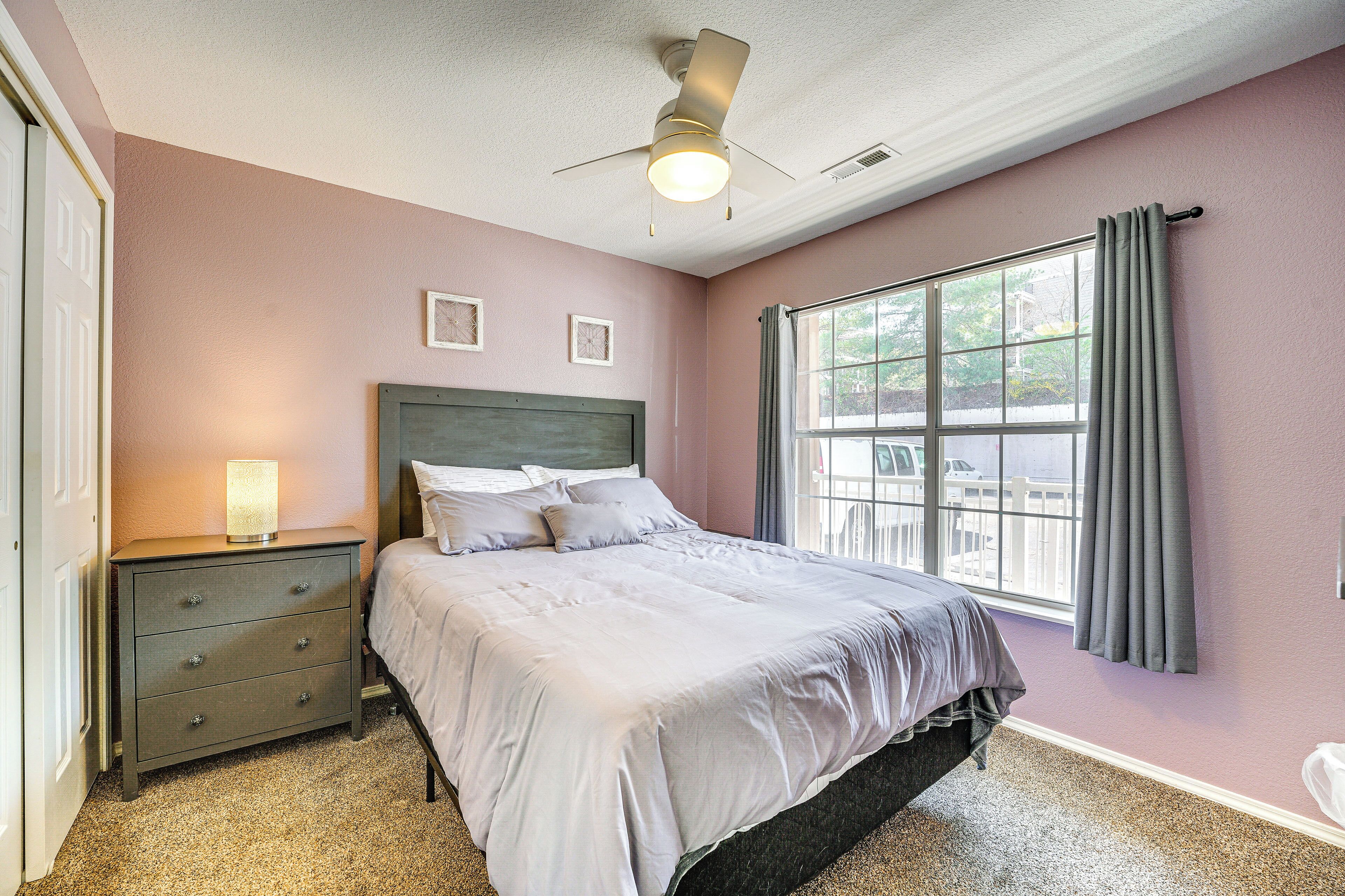 A bedroom with a bed, a nightstand, a lamp, a window with curtains, and a ceiling fan.