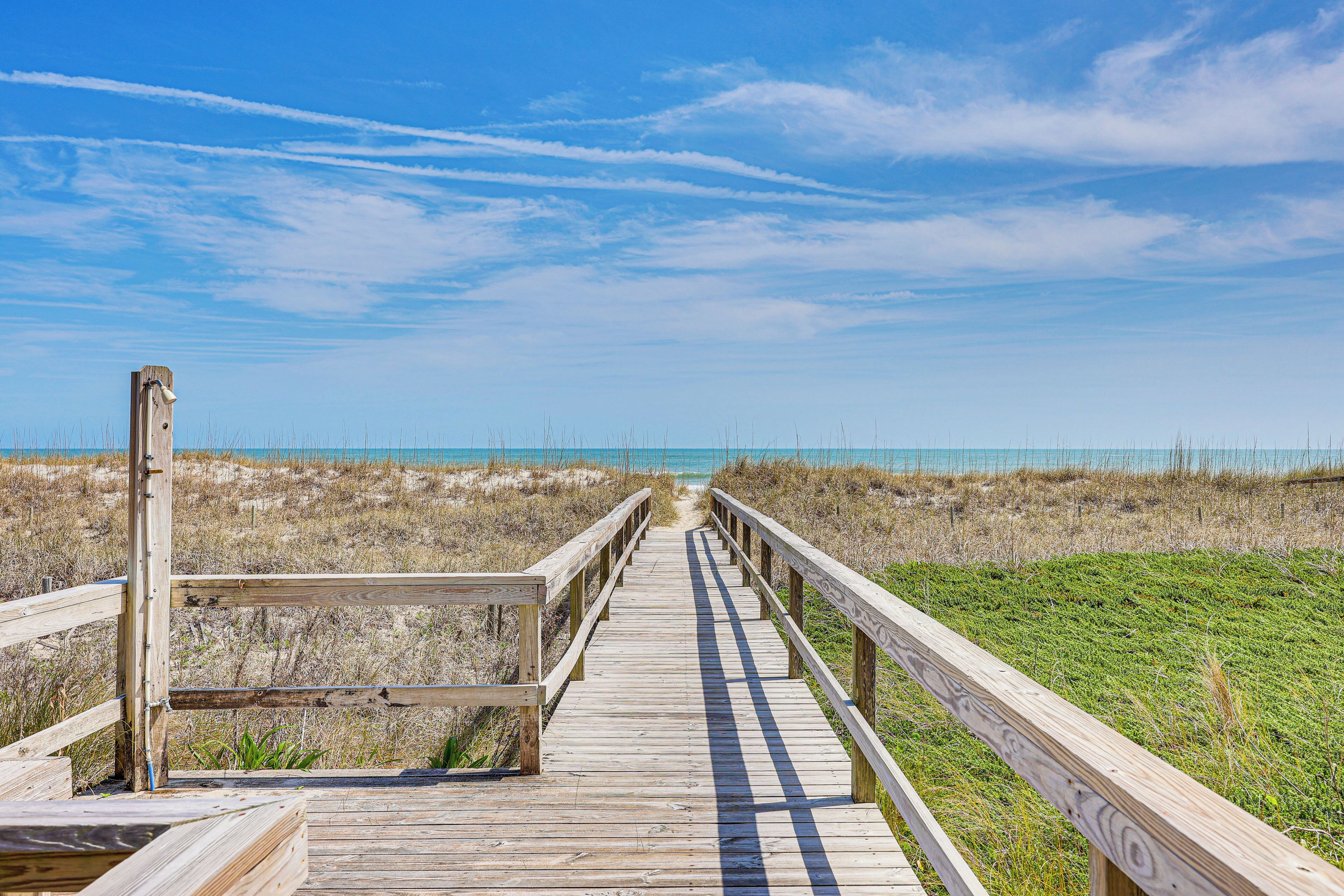A wooden boardwalk leading to a beach with a clear sky.