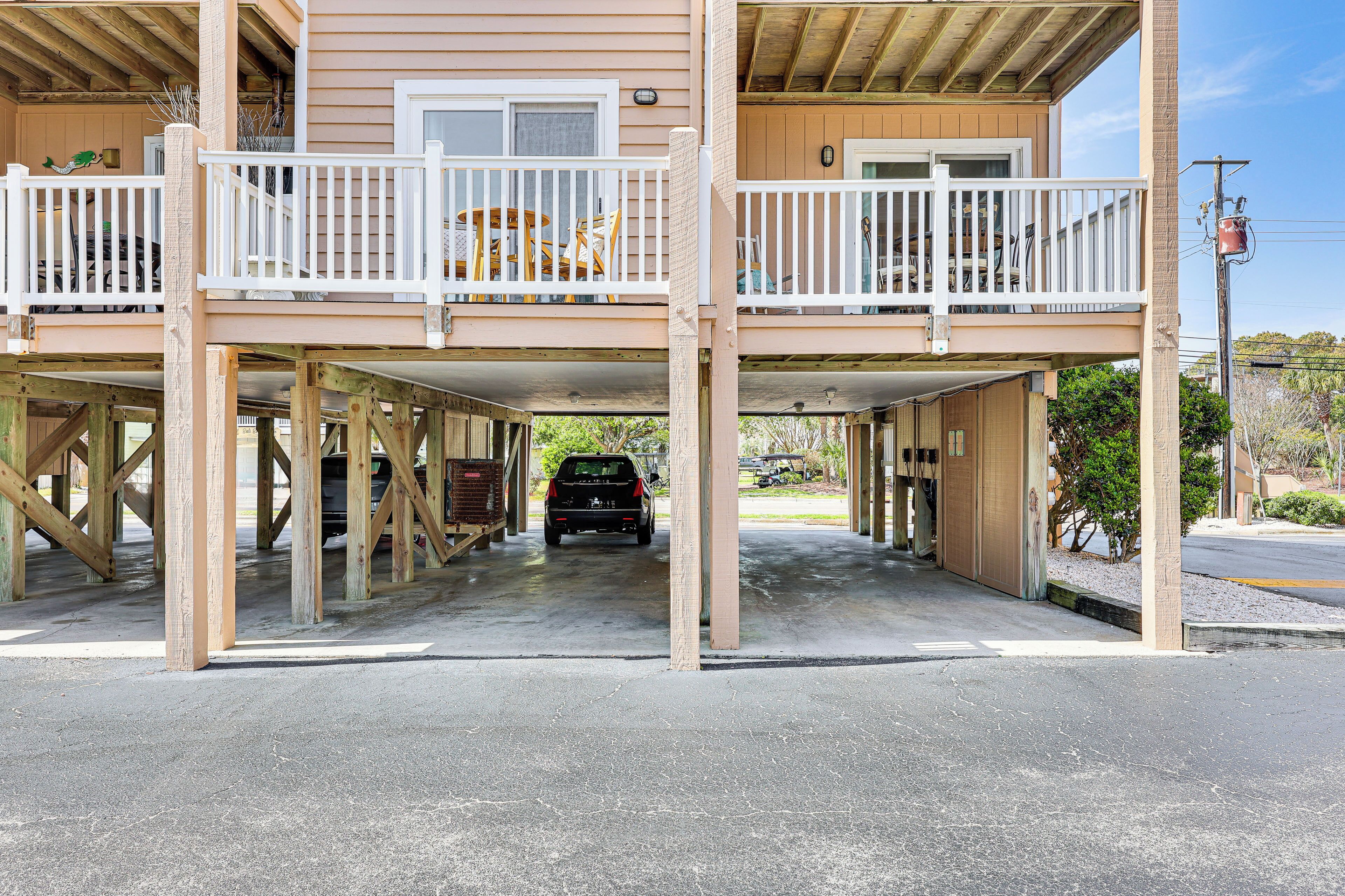 A two-story building with a covered parking area and a balcony with white railings.