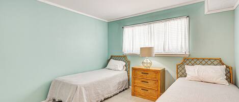 Une chambre avec deux lits simples, une table de chevet en bois avec une lampe et une fenêtre avec des rideaux.