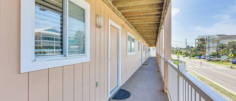 A covered outdoor corridor with a wooden ceiling, beige walls, and a metal railing.