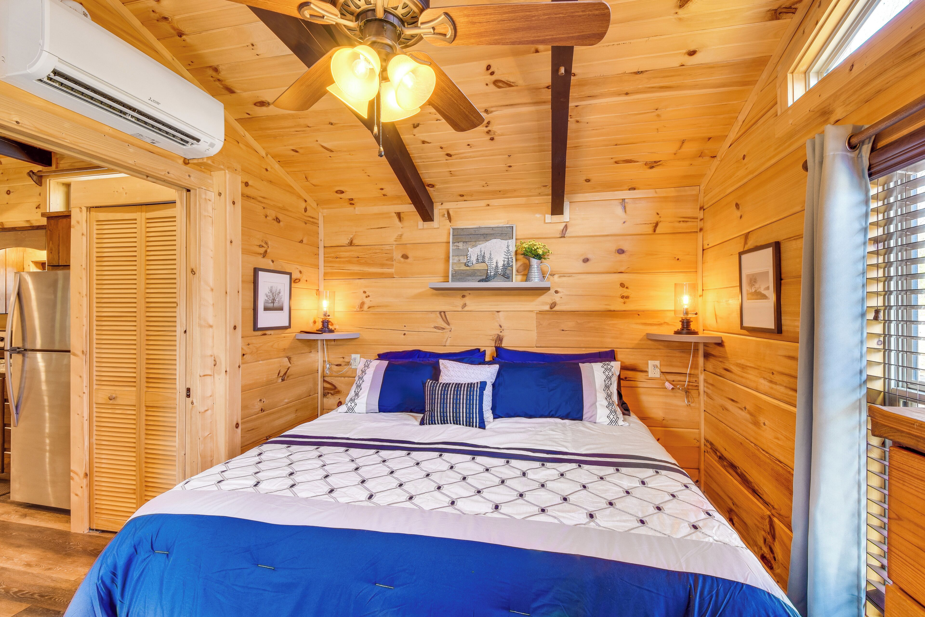 Une chambre dans une cabane en bois, équipée d’un lit, d’un ventilateur de plafond et d’un réfrigérateur.