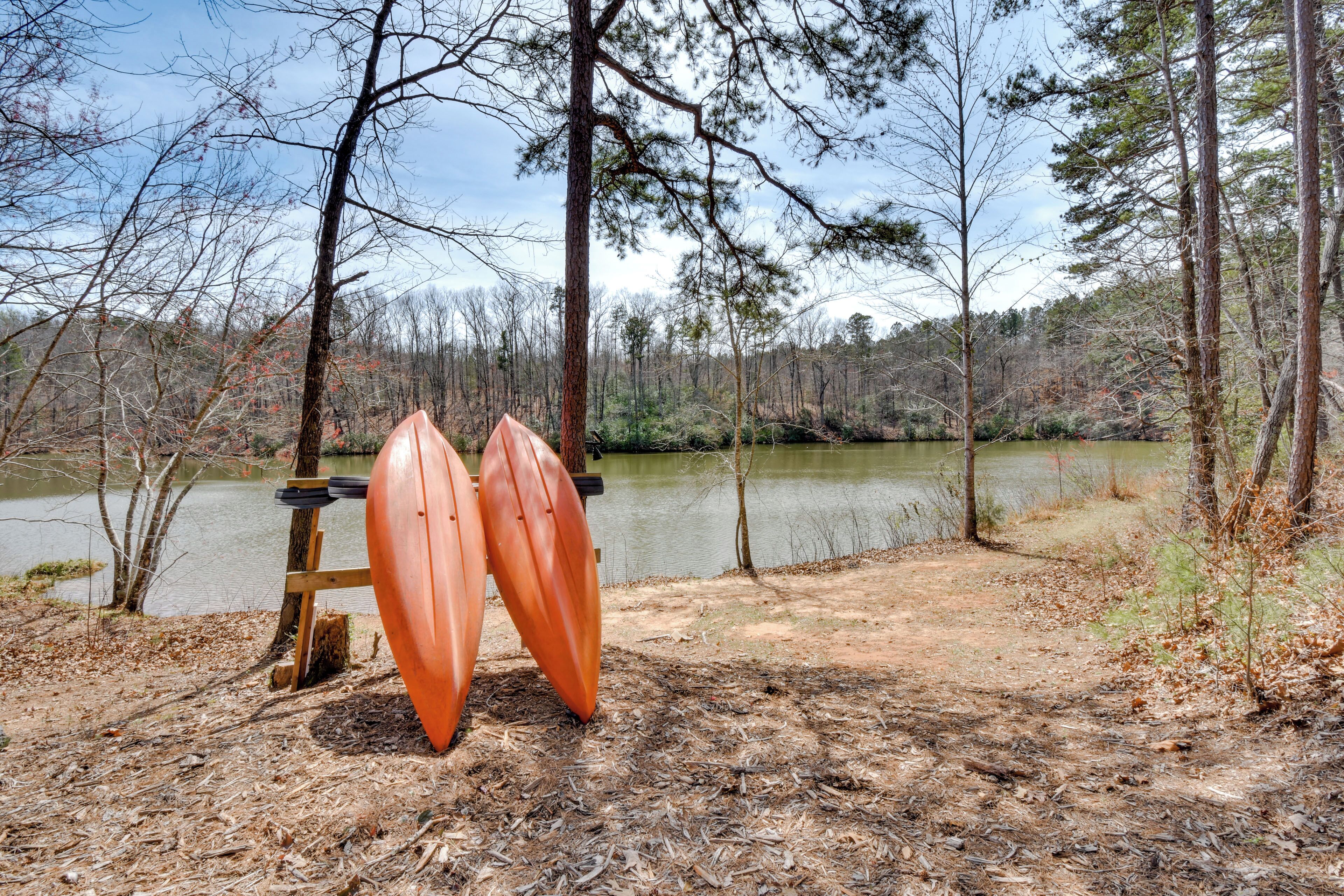 Two orange kayaks leaning against a wooden stand by a lake surrounded by trees.