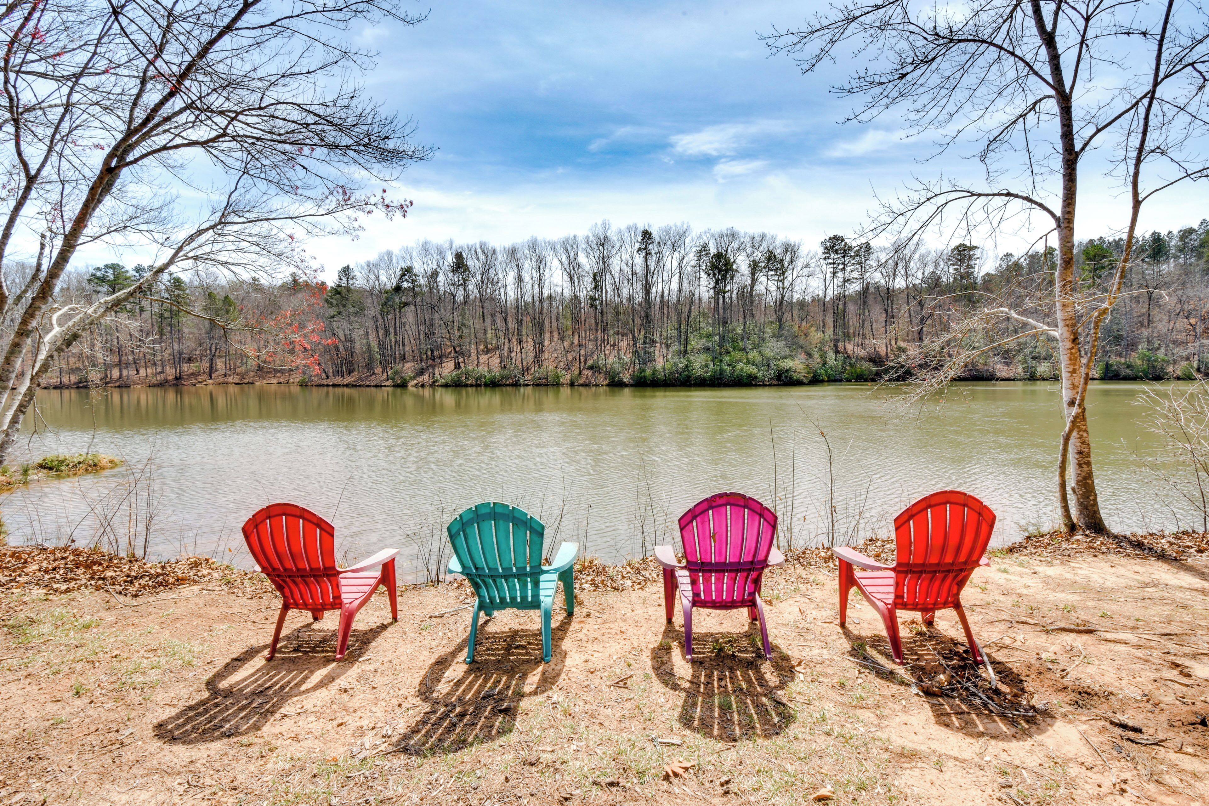 Three Adirondack chairs facing a lake with a forest in the background.