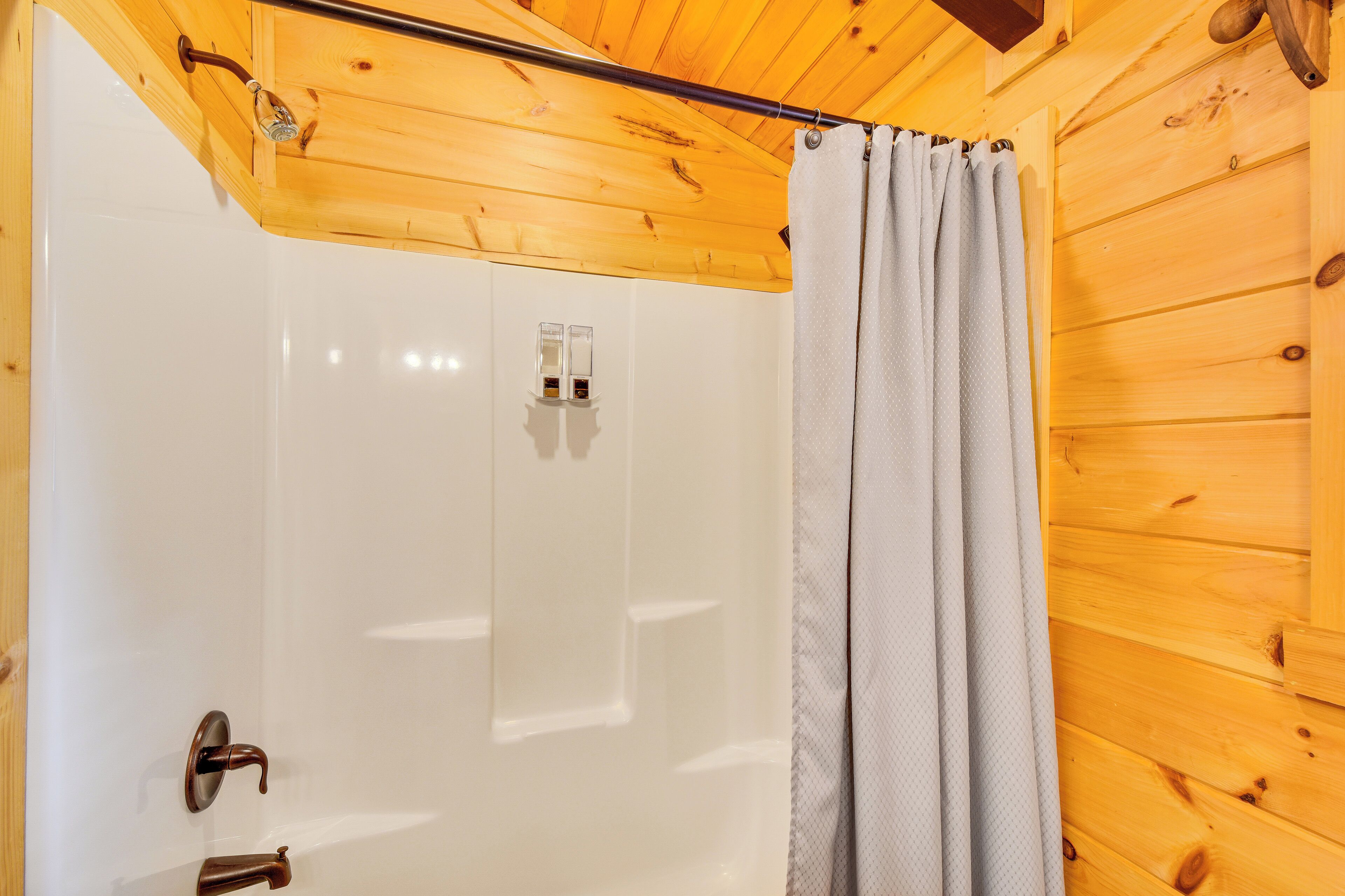 A wooden cabin interior with a shower area, a wooden ceiling, and a white door.