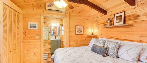 A wooden cabin bedroom with a bed, a ceiling fan, a mirror, and a shelf with a picture.