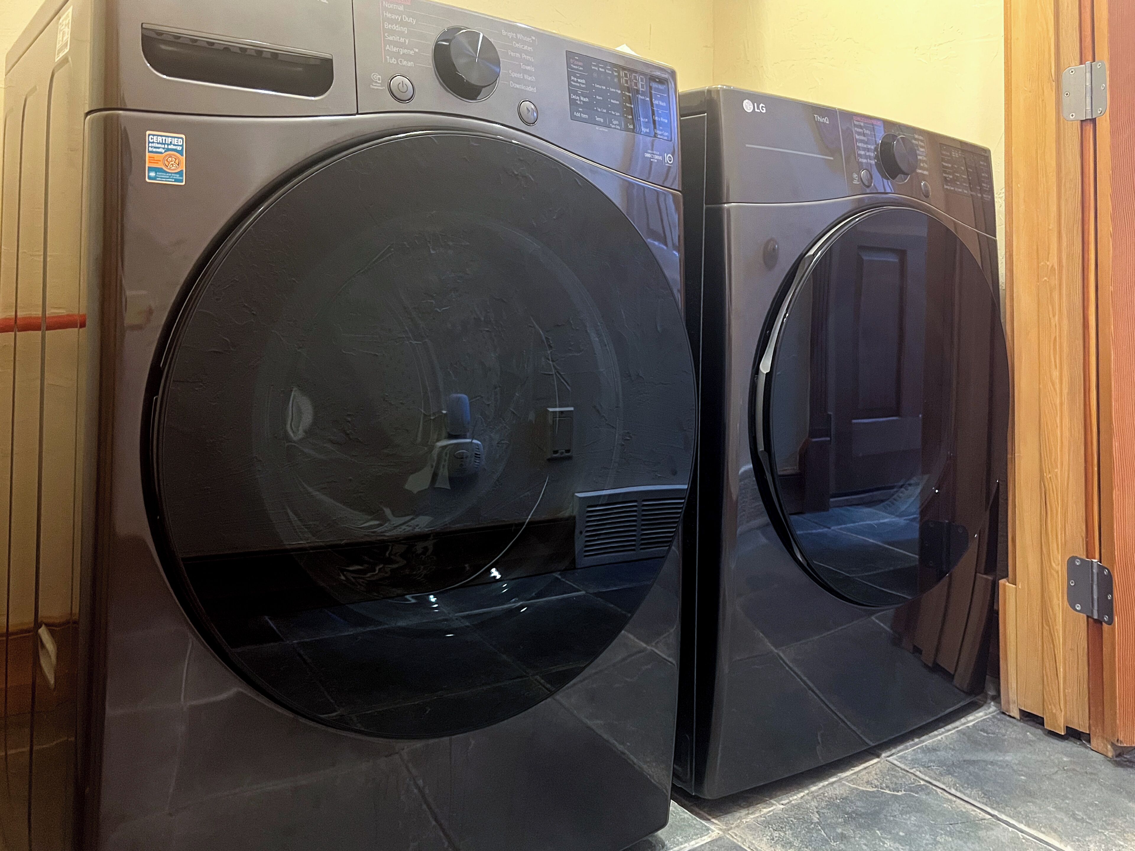 Two front-loading LG washing machines in a laundry room with tiled flooring and wooden walls.