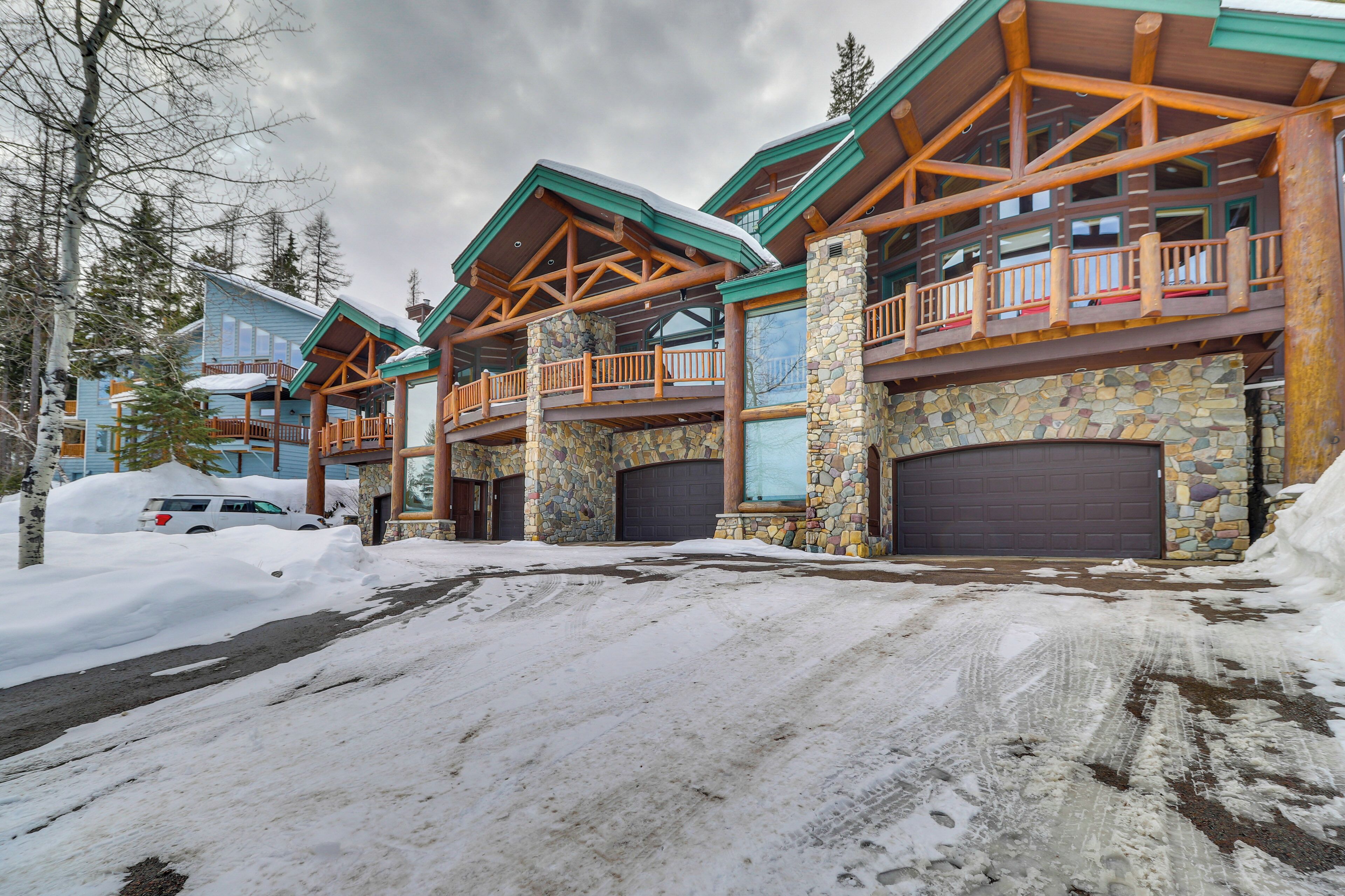 A multi-story lodge with a stone facade, wooden balconies, and a snow-covered driveway.