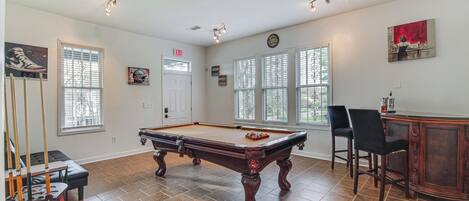 A pool table in a room with large windows, a door, and a bar area.