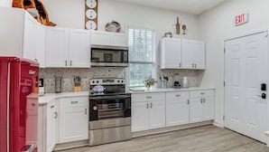 A modern kitchen with white cabinets, a red refrigerator, stainless steel appliances, and a window with blinds. - Stylish Home ~ 2 Mi to Jackson State & Belhaven! (Jackson)