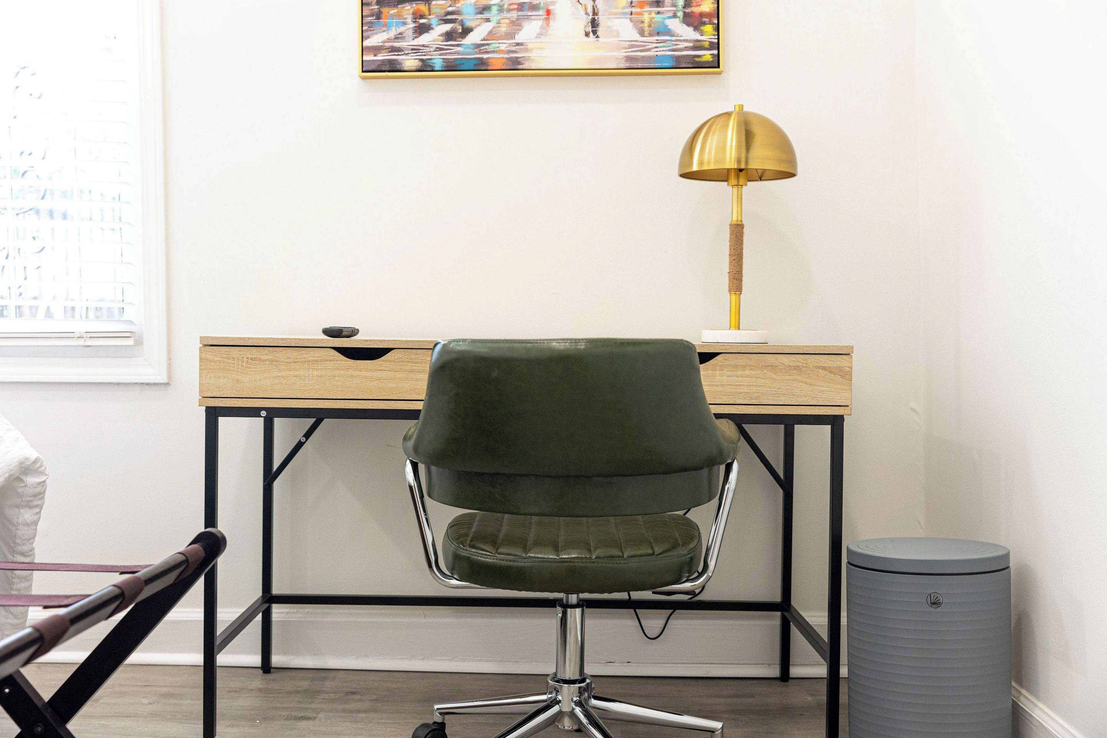 Een werkplek met een bureau, een groene stoel, een lamp en een prullenbak.