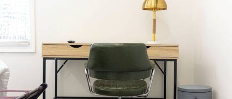 Een werkplek met een bureau, een groene stoel, een lamp en een prullenbak.